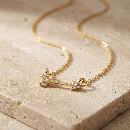 Gold necklace with an arrow pendant on a beige stone surface