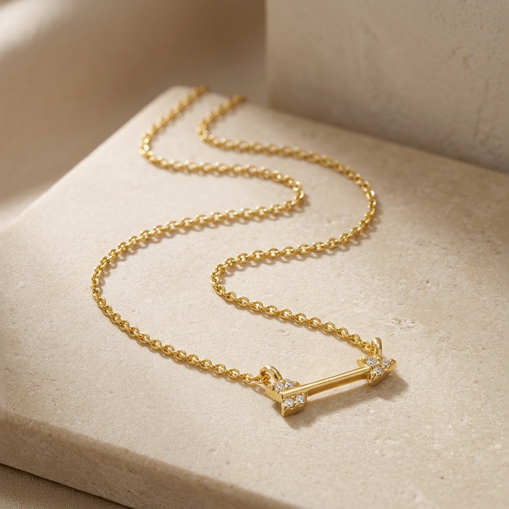 Gold necklace with an arrow-shaped pendant on a beige surface