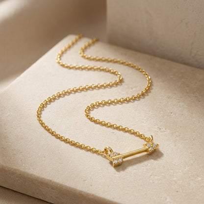 Gold necklace with an arrow-shaped pendant on a beige surface