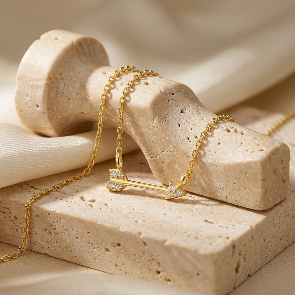 Gold necklace with an arrow pendant on a beige stone surface
