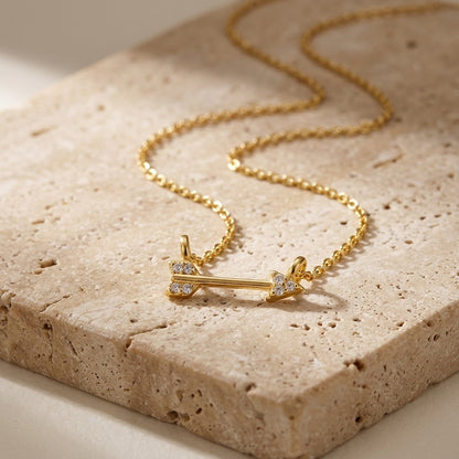 Gold necklace with an arrow pendant on a textured stone surface