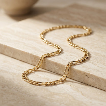 Gold chain necklace on a light sandstone surface