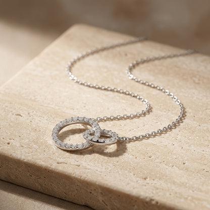 Silver necklace with interlocking rings on a beige stone surface