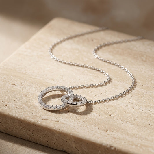 Silver necklace with interlocking rings on a beige stone surface