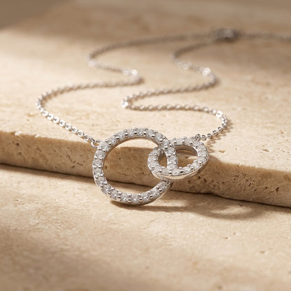 Silver necklace with interlocking rings on a beige stone surface
