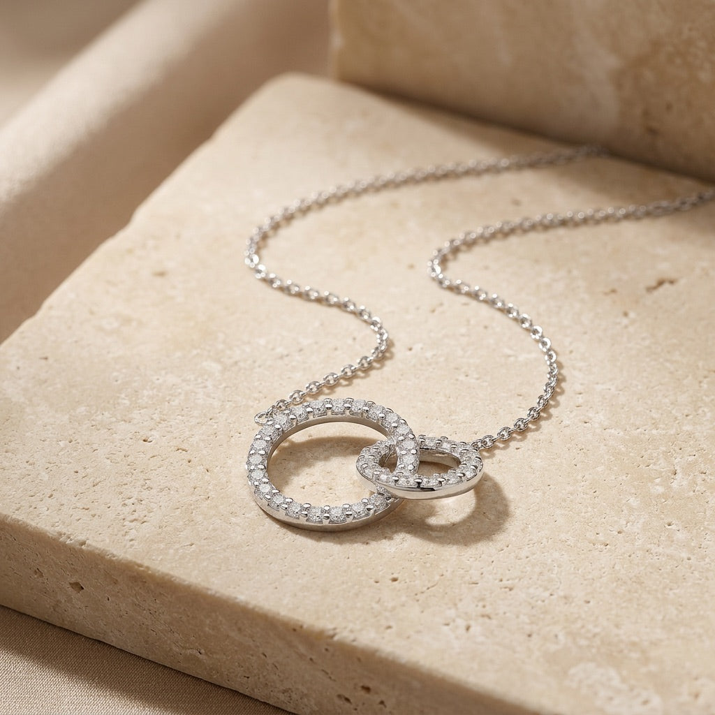 Silver necklace with interlocking rings on a beige stone surface