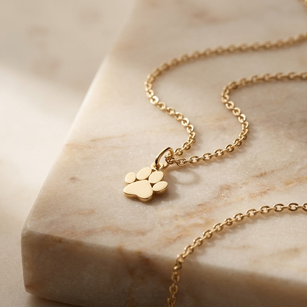 Gold necklace with a paw-shaped pendant on a marble surface