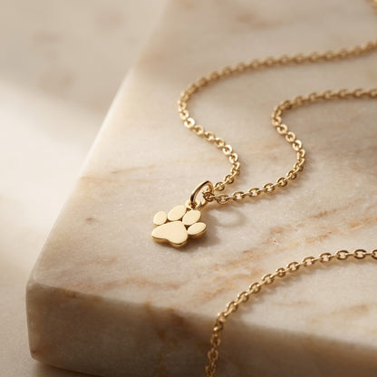 Gold necklace with a paw-shaped pendant on a marble surface