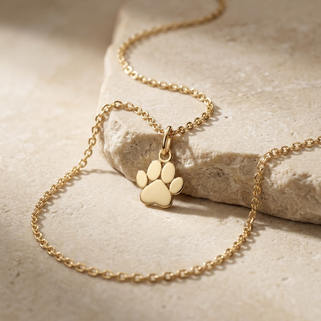 Gold necklace with a paw print pendant on a stone surface