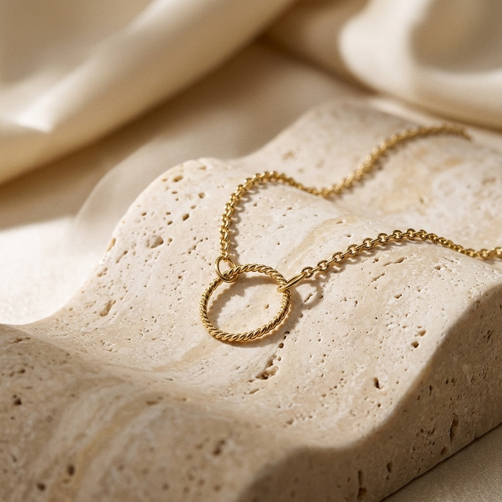 Gold necklace with a circular pendant on a textured beige surface