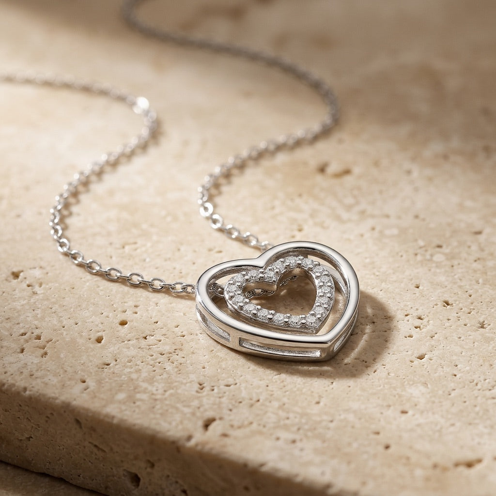 Silver heart-shaped necklace with a chain on a beige stone surface