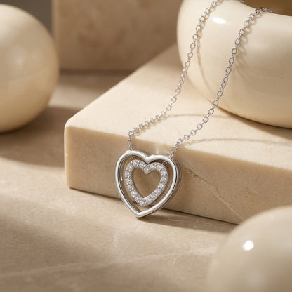 Silver heart-shaped necklace on a beige stone surface