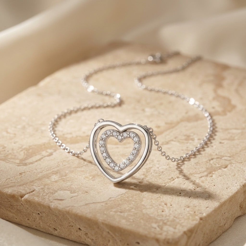 Silver heart-shaped necklace with embedded stones on a beige stone surface