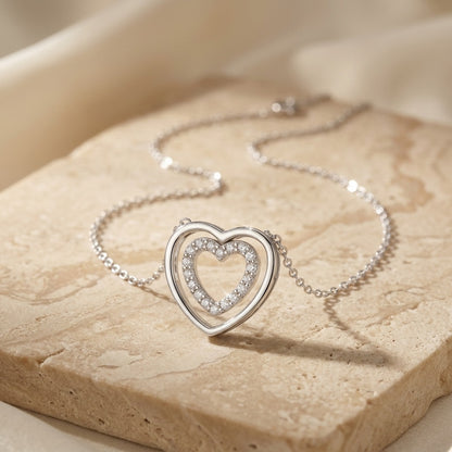 Silver heart-shaped necklace with embedded stones on a beige stone surface