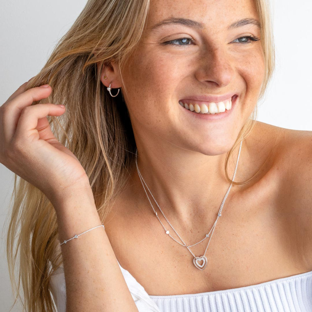 Woman wearing silver jewellery including a Cubic Zirconia Double Open Heart 18” Necklet, bracelet, and earrings on a plain background
