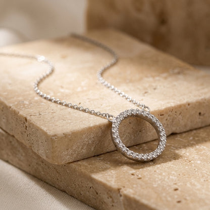 Silver necklace with a circular pendant on a beige stone surface