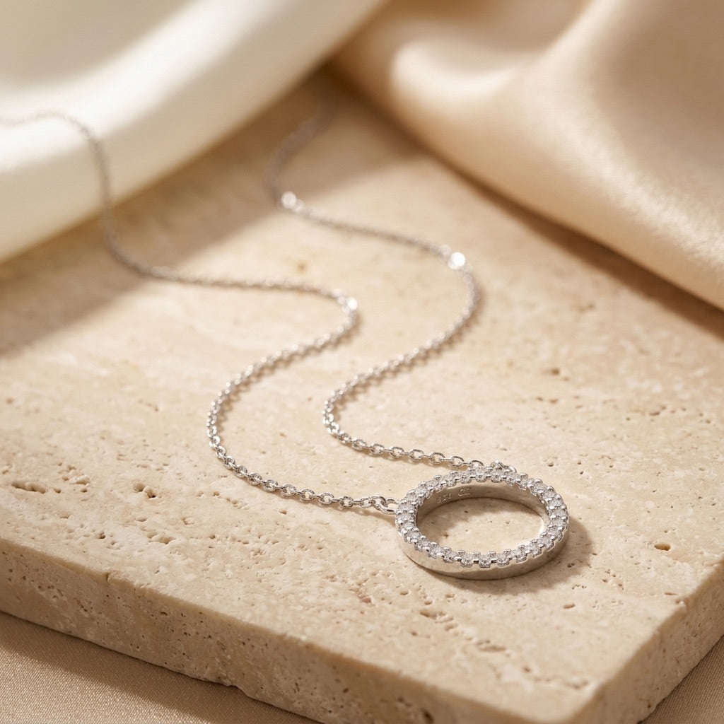 Silver necklace with a circular pendant on a beige stone surface