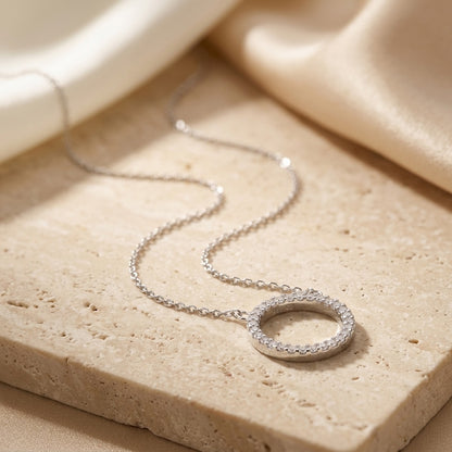 Silver necklace with a circular pendant on a beige stone surface