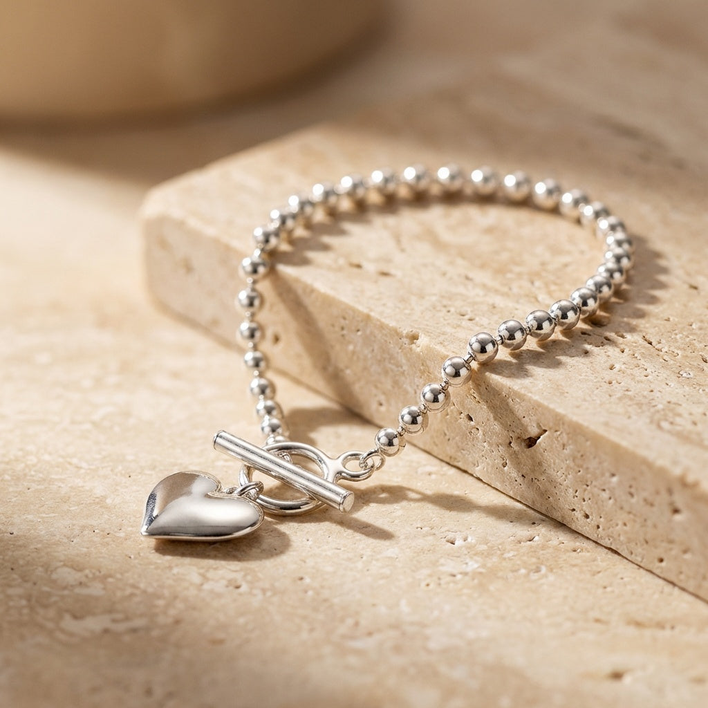 Silver bracelet with heart charm on a beige stone surface
