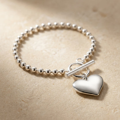 Silver beaded bracelet with a heart-shaped charm on a beige background