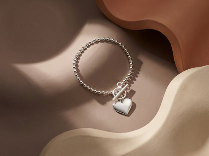 Silver bracelet with a heart charm on a wavy beige surface