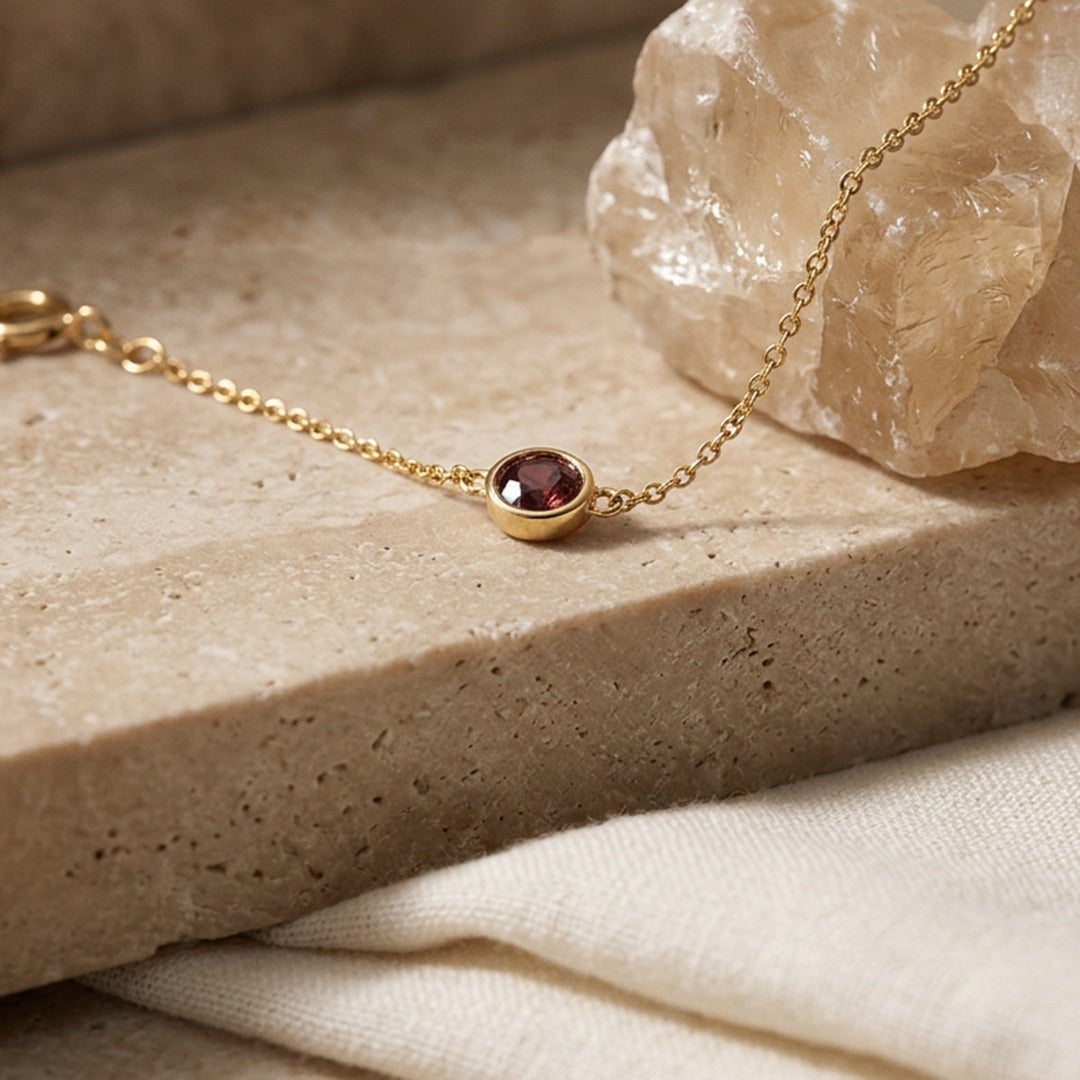 Gold bracelet with a red gemstone on a stone surface