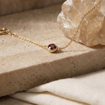 Gold bracelet with a red gemstone on a stone surface