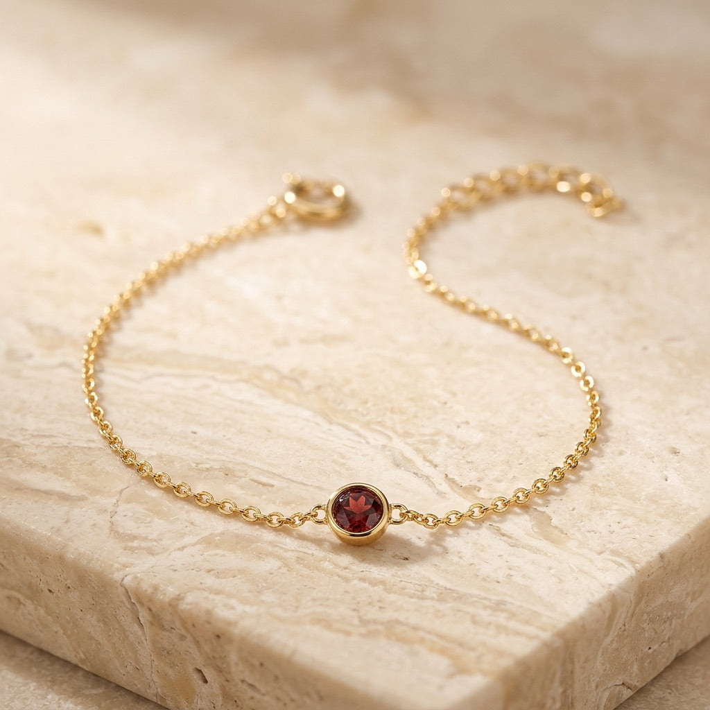 Gold bracelet with a red gemstone on a beige stone surface