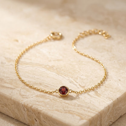 Gold bracelet with a red gemstone on a beige stone surface