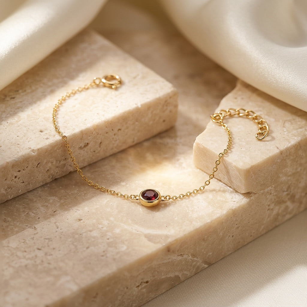 Gold bracelet with a red gemstone on a beige stone surface