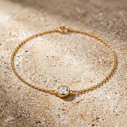 Gold bracelet with a diamond on a textured beige surface