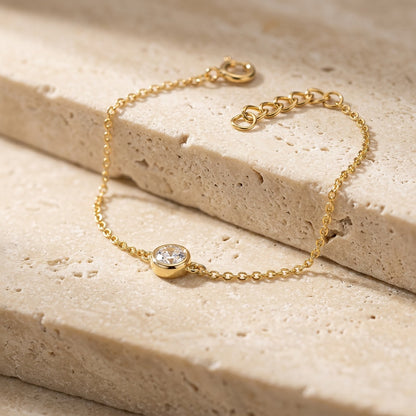 Gold bracelet with a diamond on a beige stone surface