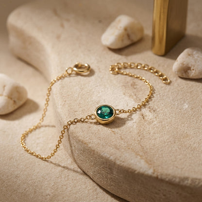 Gold bracelet with a green gemstone on a sandy surface