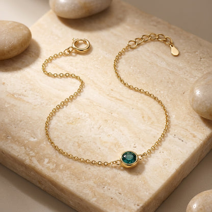 Gold bracelet with a green gemstone on a stone surface