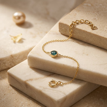 Gold bracelet with a green gemstone on a beige stone surface