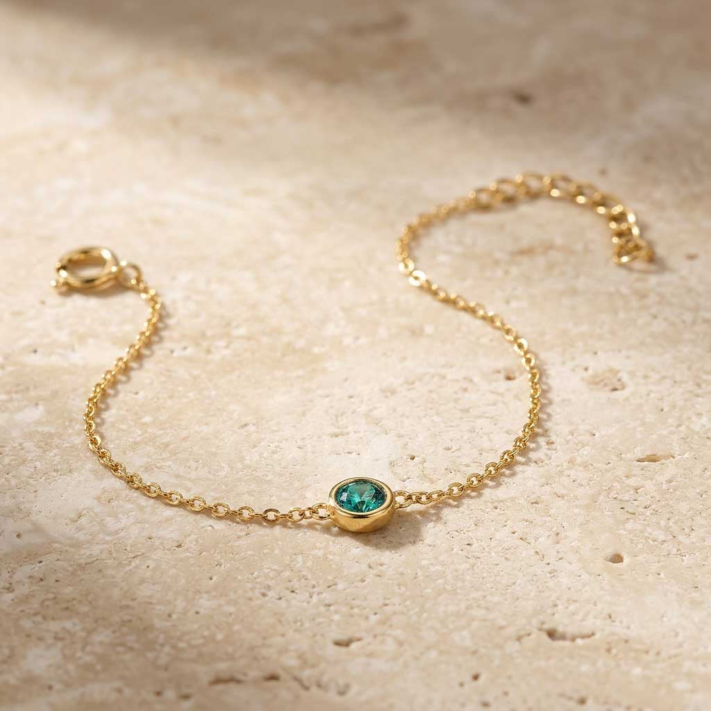 Gold bracelet with a green gemstone on a beige surface