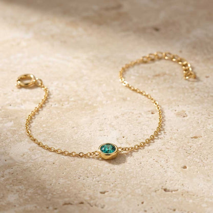 Gold bracelet with a green gemstone on a beige surface