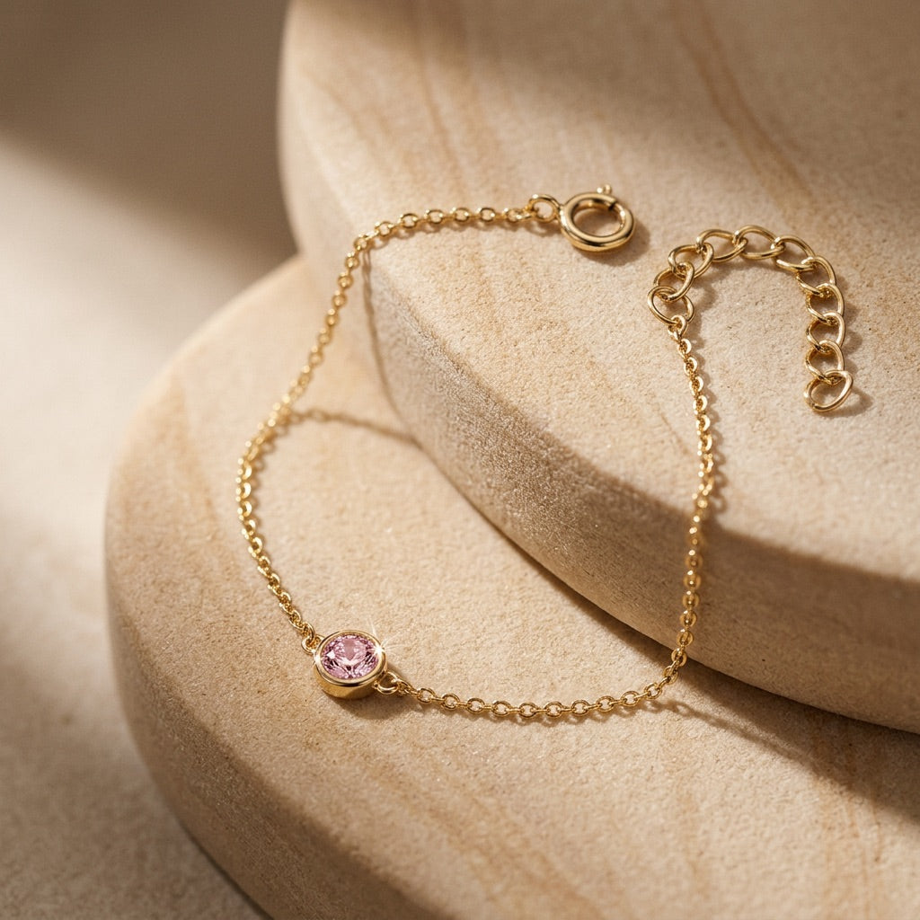 Gold bracelet with a pink gemstone on a beige stone surface