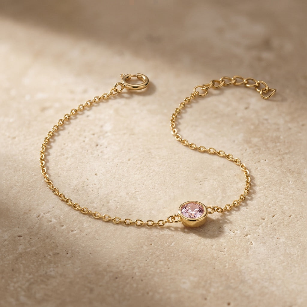 Gold bracelet with a pink gemstone on a beige surface