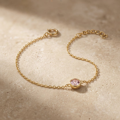 Gold bracelet with a pink gemstone on a beige surface