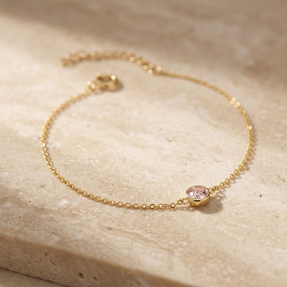 Gold bracelet with a pink gemstone on a beige stone surface