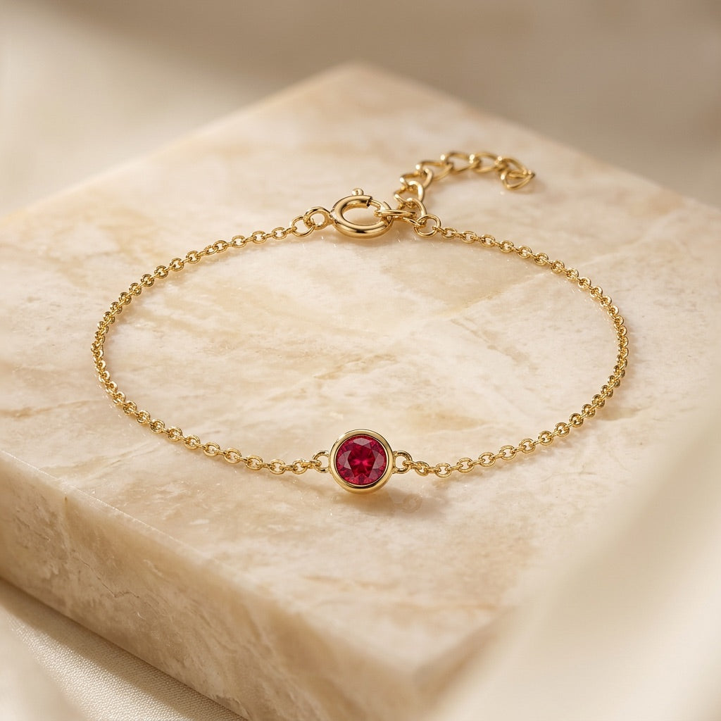 Gold bracelet with a red gemstone on a beige stone surface