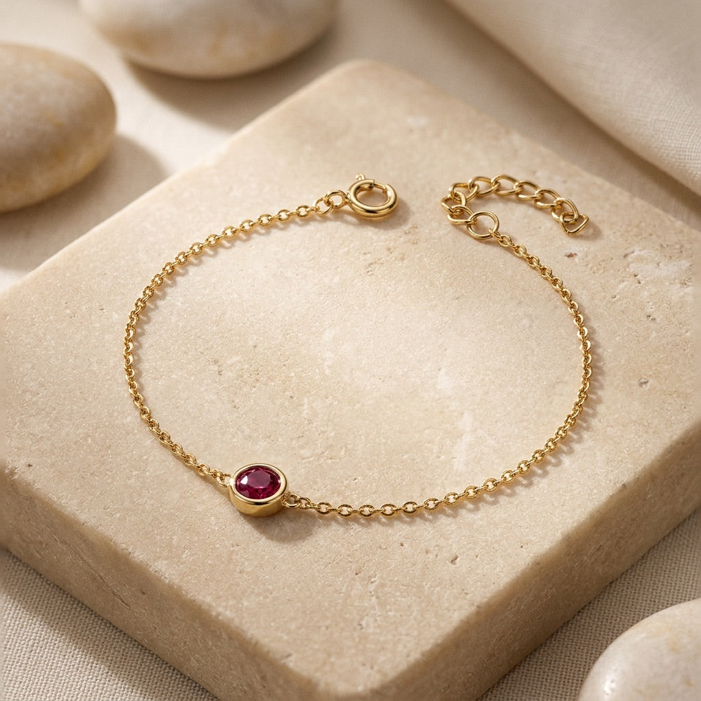Gold bracelet with a red gemstone on a beige stone surface