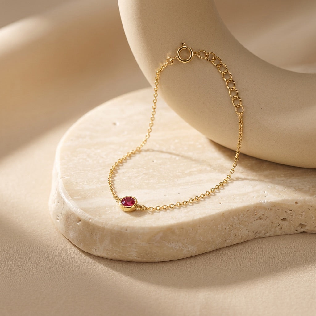 Gold bracelet with a red gemstone on a beige stone surface