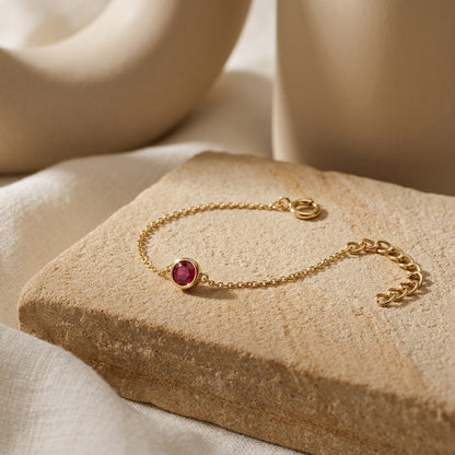 Gold bracelet with a red gemstone on a textured beige surface