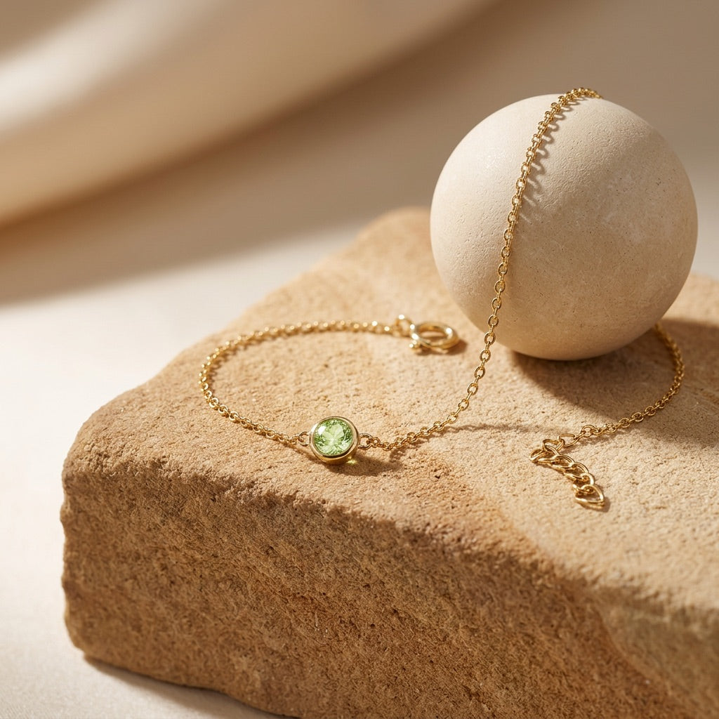 Gold bracelet with a green gemstone on a beige stone surface