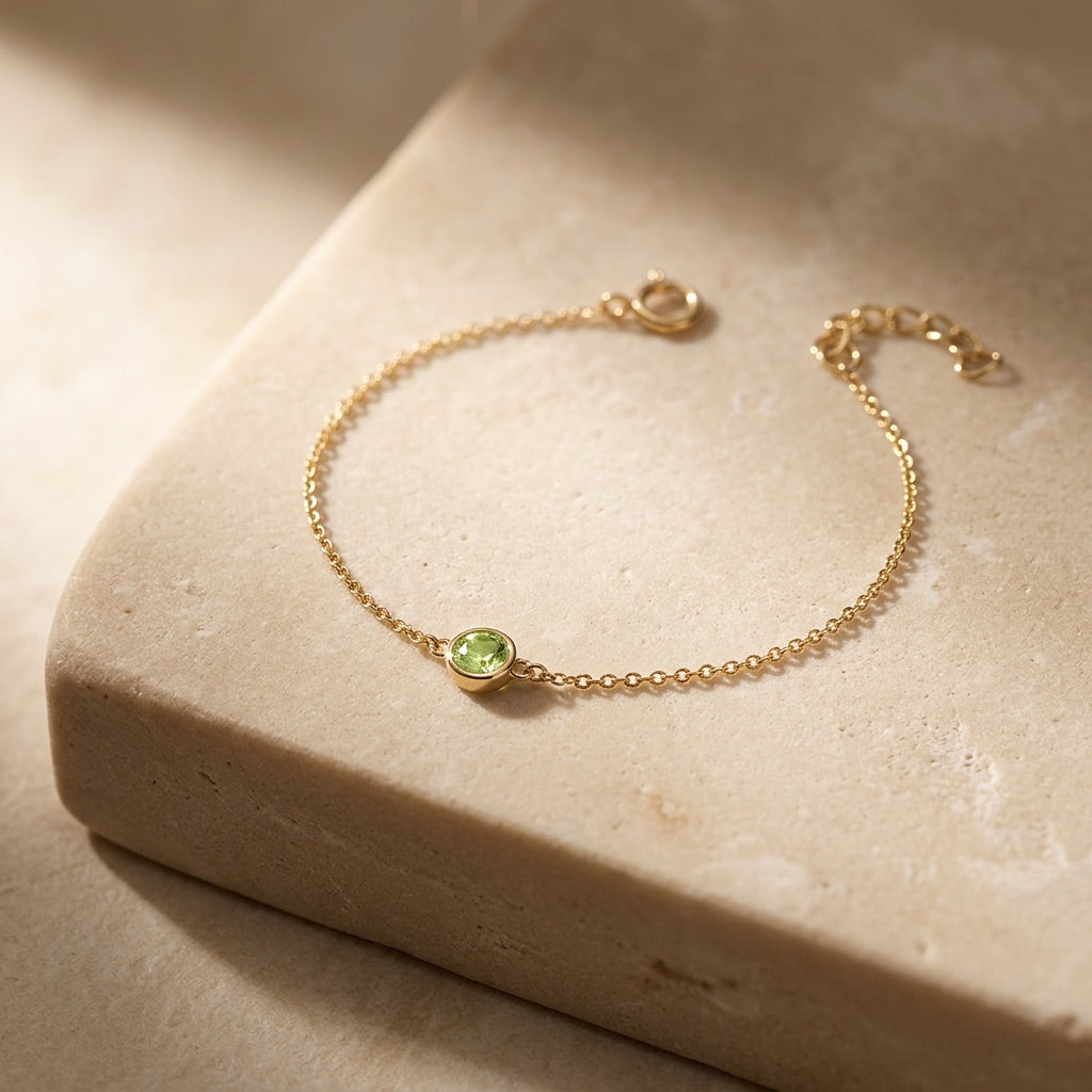 Gold bracelet with a green gemstone on a beige stone surface