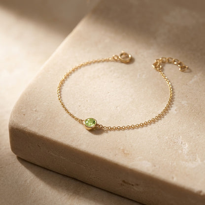 Gold bracelet with a green gemstone on a beige stone surface