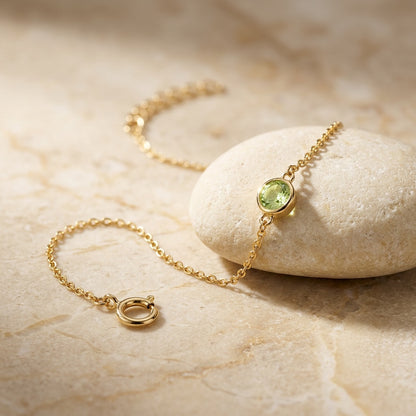 Gold bracelet with a green gemstone on a beige stone surface