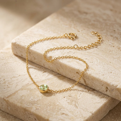 Gold bracelet with a green gemstone on a beige stone surface